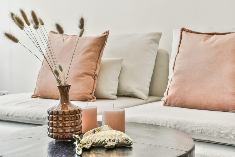 Light colored armless sofa with salmon accent pillows, pink candles and small vase
